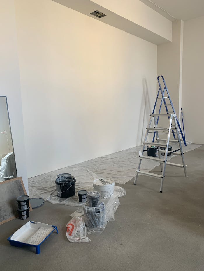 A room in the process of renovation with painting supplies and a ladder.