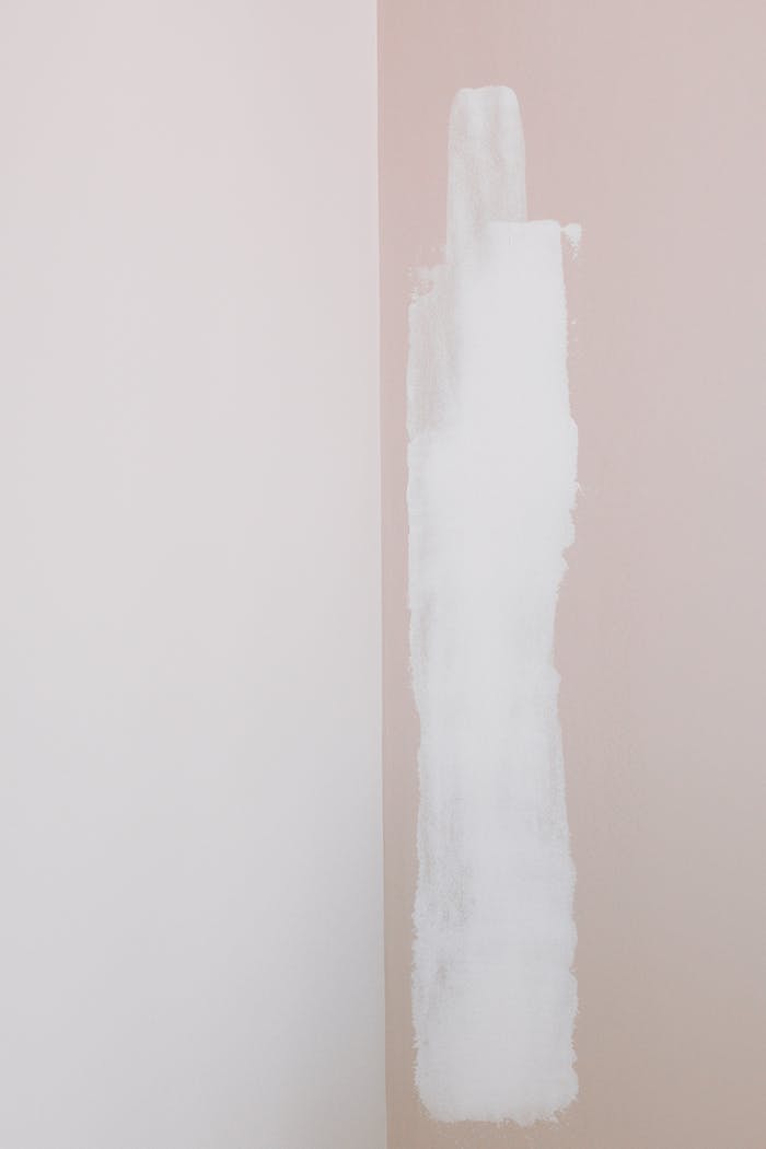 A minimalist interior with white paint on a pastel pink wall, showing home improvement in progress.
